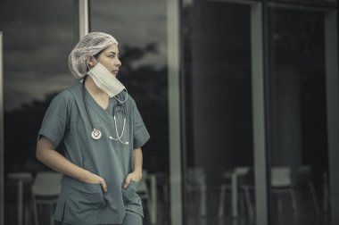 Depresyonda olan Asyalı kadın hemşire yüz maskesi giyiyor mavi üniforma hastane zemininde oturuyor, genç kadın doktor sıkı çalışmaktan strese giriyor.