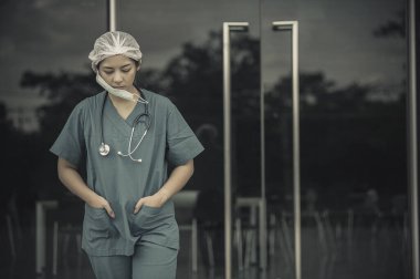 Depresyonda olan Asyalı kadın hemşire yüz maskesi giyiyor mavi üniforma hastane zemininde oturuyor, genç kadın doktor sıkı çalışmaktan strese giriyor.