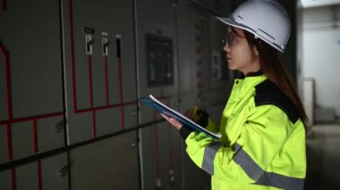 Asyalı elektrik mühendisi kontrol odasındaki elektrik sistemini kontrol etmek ve izlemek için pano tutuyor.