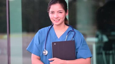 Depresyonda olan Asyalı hemşire kadın yüz maskesi takıyor ve hastane yakınlarında mavi üniforma giyiyor. Genç bayan doktor sıkı çalışmanın stresi altında