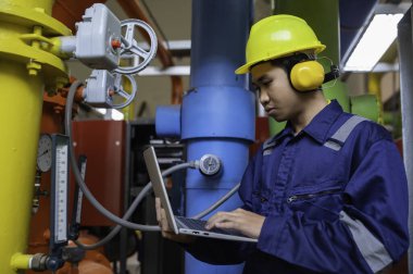 Isıtma tesisinde bakım teknisyeni. Petrokimya işçisi fabrikadaki gaz ve petrol boru hatlarının işletilmesini denetliyor. Mühendis işitme koruyucuyu birçok boruyla aynı odaya koydu.