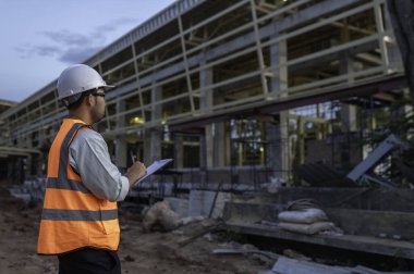 Büyük bir inşaat projesinin şantiyesinde çalışan Asyalı mühendis. Taylandlılar. İnşaat alanında fazla mesai