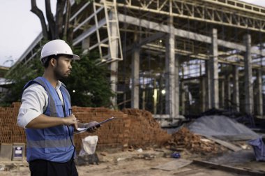 Büyük bir inşaat projesinin şantiyesinde çalışan Asyalı mühendis. Taylandlılar. İnşaat alanında fazla mesai