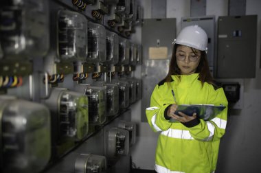 Asyalı elektrik mühendisi kontrol odasındaki elektrik sistemini kontrol etmek ve izlemek için pano tutuyor. Tayland teknisyeni ve çalışanlar