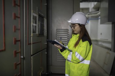 Asyalı elektrik mühendisi kontrol odasındaki elektrik sistemini kontrol etmek ve izlemek için pano tutuyor. Tayland teknisyeni ve çalışanlar