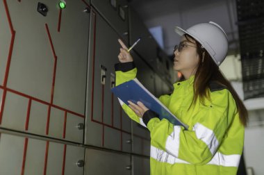 Asyalı elektrik mühendisi kontrol odasındaki elektrik sistemini kontrol etmek ve izlemek için pano tutuyor. Tayland teknisyeni ve çalışanlar