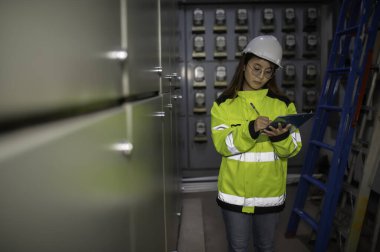 Asyalı elektrik mühendisi kontrol odasındaki elektrik sistemini kontrol etmek ve izlemek için pano tutuyor. Tayland teknisyeni ve çalışanlar