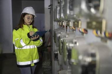 Asyalı elektrik mühendisi kontrol odasındaki elektrik sistemini kontrol etmek ve izlemek için pano tutuyor. Tayland teknisyeni ve çalışanlar