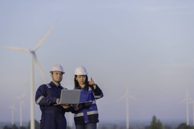 İki mühendis dağdaki rüzgar türbini çiftliği güç jeneratörü istasyonunda çalışıyor ve raporu tutuyor. Taylandlılar. Teknisyen ve kadın iş hakkında tartışıyorlar.