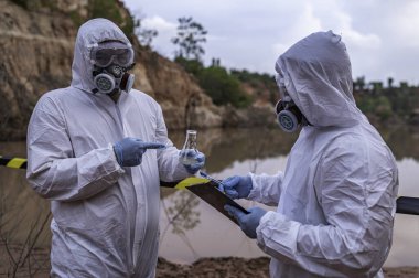 Su analizi üzerinde çalışan koruyucu üniforma giyen bilim adamları ya da biyologlar. Çevre mühendisleri tehlikeli alanlarda su kalitesini kontrol ederler.