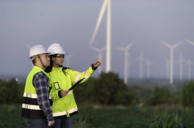 İki mühendis dağdaki rüzgar türbini çiftliği güç jeneratörü istasyonunda çalışıyor ve raporu tutuyor. Taylandlılar. Teknisyen ve kadın iş hakkında tartışıyorlar.