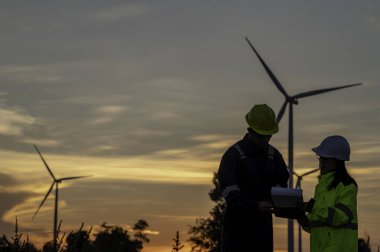 İki mühendis dağdaki rüzgar türbini çiftliği güç jeneratörü istasyonunda çalışıyor ve raporu tutuyor. Taylandlılar. Teknisyen ve kadın iş hakkında tartışıyorlar.
