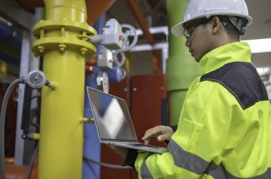 Kazan dairesinde çalışan gözlüklü Asyalı mühendis ısıtma sistemi ekipmanlarının teknik verilerini kontrol ediyor. Taylandlılar.