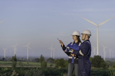 İki mühendis dağdaki rüzgar türbini çiftliği güç jeneratörü istasyonunda çalışıyor ve raporu tutuyor. Taylandlılar. Teknisyen ve kadın iş hakkında tartışıyorlar.