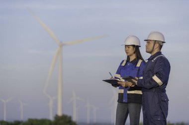 İki mühendis dağdaki rüzgar türbini çiftliği güç jeneratörü istasyonunda çalışıyor ve raporu tutuyor. Taylandlılar. Teknisyen ve kadın iş hakkında tartışıyorlar.