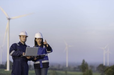 İki mühendis dağdaki rüzgar türbini çiftliği güç jeneratörü istasyonunda çalışıyor ve raporu tutuyor. Taylandlılar. Teknisyen ve kadın iş hakkında tartışıyorlar.