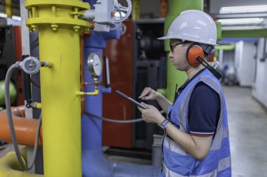 Isıtma tesisinde bakım teknisyeni. Petrokimya işçisi fabrikadaki gaz ve petrol boru hatlarının işletilmesini denetliyor. Mühendis işitme koruyucuyu birçok boruyla aynı odaya koydu.