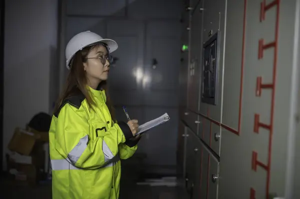 Asian electric engineer holding clipboard for checking and monitoring the electrical system in the control room. Technician thailand people working
