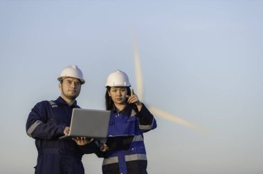 İki mühendis dağdaki rüzgar türbini çiftliği güç jeneratörü istasyonunda çalışıyor ve raporu tutuyor. Taylandlılar. Teknisyen ve kadın iş hakkında tartışıyorlar.