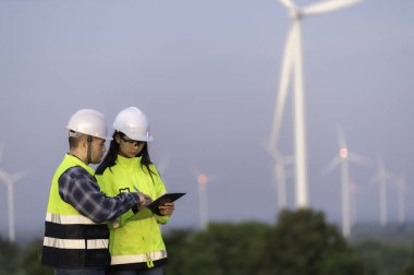 İki mühendis dağdaki rüzgar türbini çiftliği güç jeneratörü istasyonunda çalışıyor ve raporu tutuyor. Taylandlılar. Teknisyen ve kadın iş hakkında tartışıyorlar.