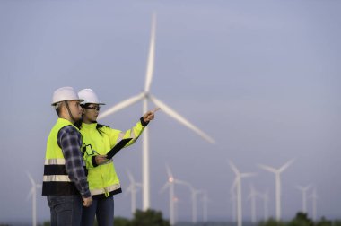 İki mühendis dağdaki rüzgar türbini çiftliği güç jeneratörü istasyonunda çalışıyor ve raporu tutuyor. Taylandlılar. Teknisyen ve kadın iş hakkında tartışıyorlar.