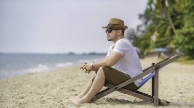 Deniz sahilinde oturan Asyalı adam. Yazın dinlenme zamanı.