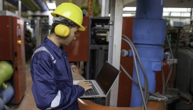 Isıtma tesisinde bakım teknisyeni. Petrokimya işçisi fabrikadaki gaz ve petrol boru hatlarının işletilmesini denetliyor. Mühendis işitme koruyucuyu birçok boruyla aynı odaya koydu.