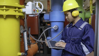 Isıtma tesisinde bakım teknisyeni. Petrokimya işçisi fabrikadaki gaz ve petrol boru hatlarının işletilmesini denetliyor. Mühendis işitme koruyucuyu birçok boruyla aynı odaya koydu.