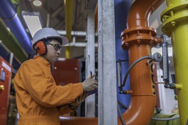 Isıtma tesisinde bakım teknisyeni. Petrokimya işçisi fabrikadaki gaz ve petrol boru hatlarının işletilmesini denetliyor. Mühendis işitme koruyucuyu birçok boruyla aynı odaya koydu.