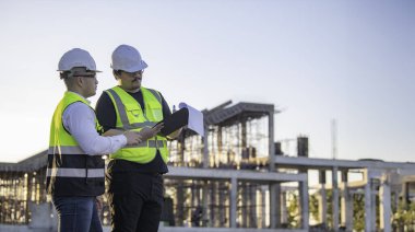 Büyük bir inşaat projesinde çalışan iki Asyalı mühendis. Taylandlılar. İnşaat alanında fazla mesai yapıyorum. Mühendislerden oluşan bir ekip olay yerinde...