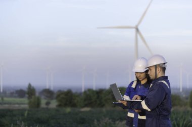 İki mühendis dağdaki rüzgar türbini çiftliği güç jeneratörü istasyonunda çalışıyor ve raporu tutuyor. Taylandlılar. Teknisyen ve kadın iş hakkında tartışıyorlar.