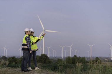 İki mühendis dağdaki rüzgar türbini çiftliği güç jeneratörü istasyonunda çalışıyor ve raporu tutuyor. Taylandlılar. Teknisyen ve kadın iş hakkında tartışıyorlar.