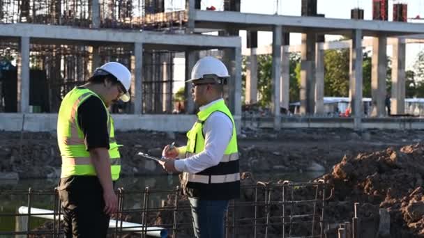Två Asiatiska Ingenjörer Som Arbetar Platsen För Ett Stort Byggnadsprojekt — Stockvideo