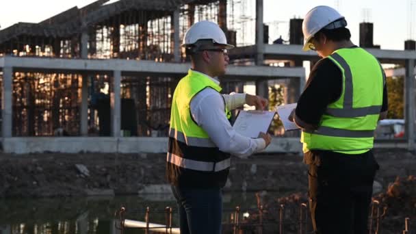 2人のアジア人エンジニアが大規模なビルプロジェクトの現場で働いている タイの人々 建設現場で残業する 現場の建築家ディスカスのチーム — ストック動画