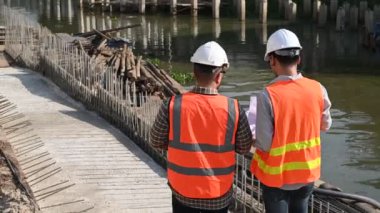 İnşaat mühendisleri nehrin üzerinde köprü inşaatında çalışıyor. İnşaat mühendisleri işleri denetliyor. Ustabaşı inşaat alanında çalışıyor.