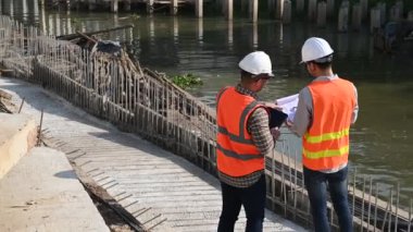 İnşaat mühendisleri nehrin üzerinde köprü inşaatında çalışıyor. İnşaat mühendisleri işleri denetliyor. Ustabaşı inşaat alanında çalışıyor.