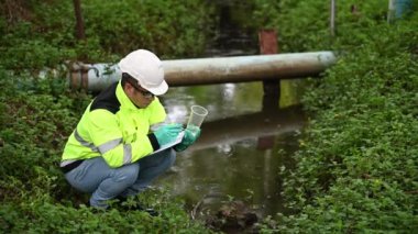 Koruyucu giysili ve koruyucu eldivenli genç adam su kirliliği seviyesini sıvılarda test ediyor