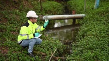 Koruyucu giysili ve koruyucu eldivenli genç adam su kirliliği seviyesini sıvılarda test ediyor