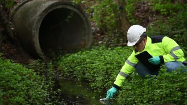 Koruyucu giysili ve koruyucu eldivenli genç adam su kirliliği seviyesini sıvılarda test ediyor