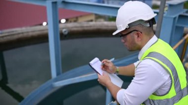 Miğferli mühendis ve bardaklar su ikmali üzerinde çalışıyor. Panoya not alıyor. Atık su kavramı