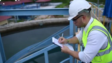 Miğferli mühendis ve bardaklar su ikmali üzerinde çalışıyor. Panoya not alıyor. Atık su kavramı