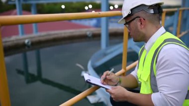 Miğferli mühendis ve bardaklar su ikmali üzerinde çalışıyor. Panoya not alıyor. Atık su kavramı