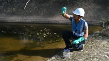 Korumalı miğferli Asyalı adam, su kaynaklarındaki kirleticileri kontrol etmek ve su testinin sonuçlarını yeniden kullanmak için su kaynaklarında çalışıyor..