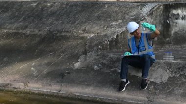 Korumalı miğferli Asyalı adam, su kaynaklarındaki kirleticileri kontrol etmek ve su testinin sonuçlarını yeniden kullanmak için su kaynaklarında çalışıyor..