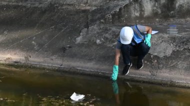 Korumalı miğferli Asyalı adam, su kaynaklarındaki kirleticileri kontrol etmek ve su testinin sonuçlarını yeniden kullanmak için su kaynaklarında çalışıyor..