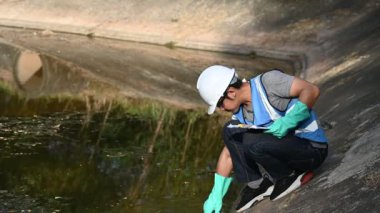 Korumalı miğferli Asyalı adam, su kaynaklarındaki kirleticileri kontrol etmek ve su testinin sonuçlarını yeniden kullanmak için su kaynaklarında çalışıyor..