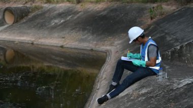 Korumalı miğferli Asyalı adam, su kaynaklarındaki kirleticileri kontrol etmek ve su testinin sonuçlarını yeniden kullanmak için su kaynaklarında çalışıyor..