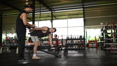 Yakışıklı adam spor salonunda antrenörle egzersiz yapıyor.