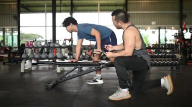 Genç adam spor salonunda antrenörle egzersiz yapıyor.