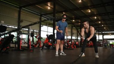 Genç adam spor salonunda antrenörle egzersiz yapıyor.